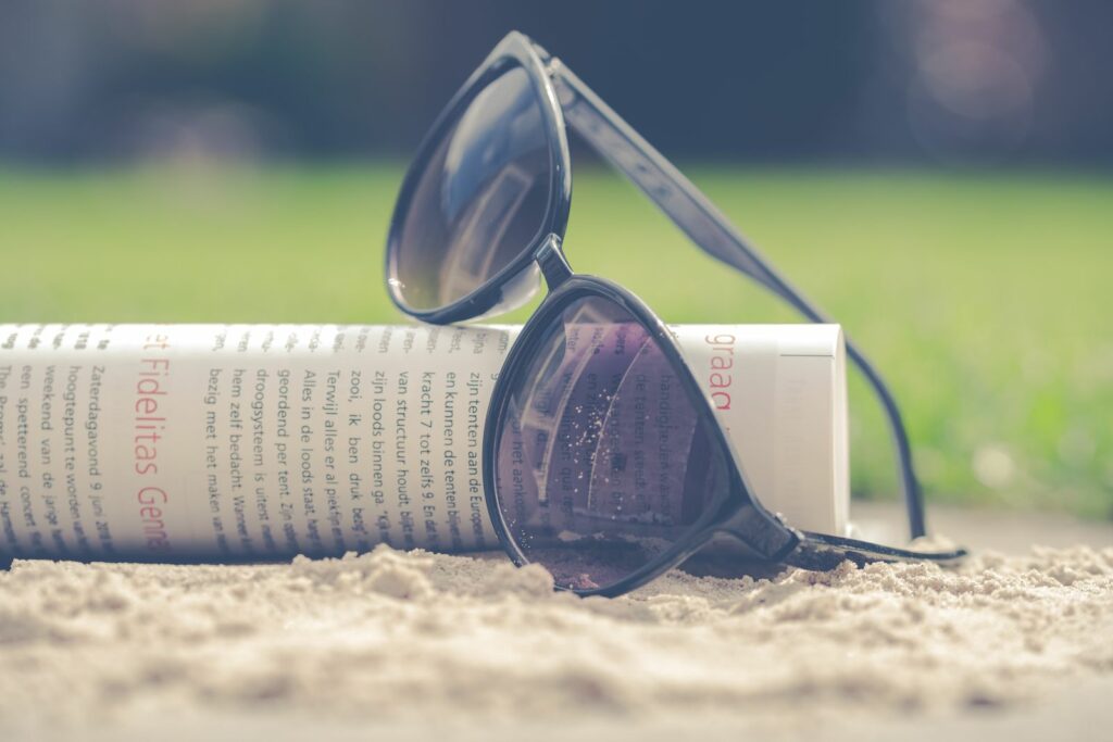 Lunettes de soleil posées sur le sable à côté d'un journal roulé