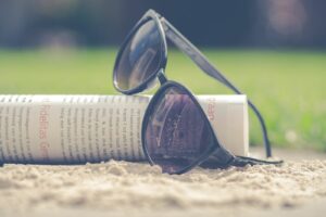 Lunettes de soleil posées sur le sable à côté d'un journal roulé